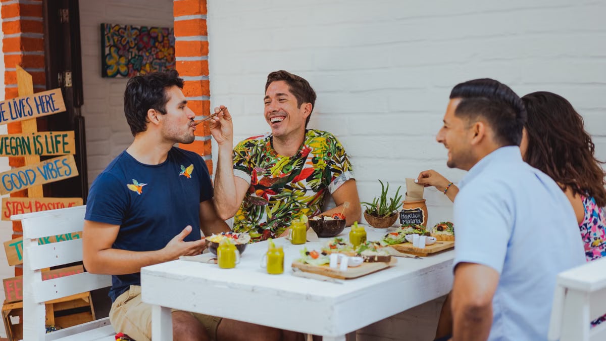 Group of friends having a fun meal outdoors at a vegan cafe, sharing laughter and vibrant dishes.